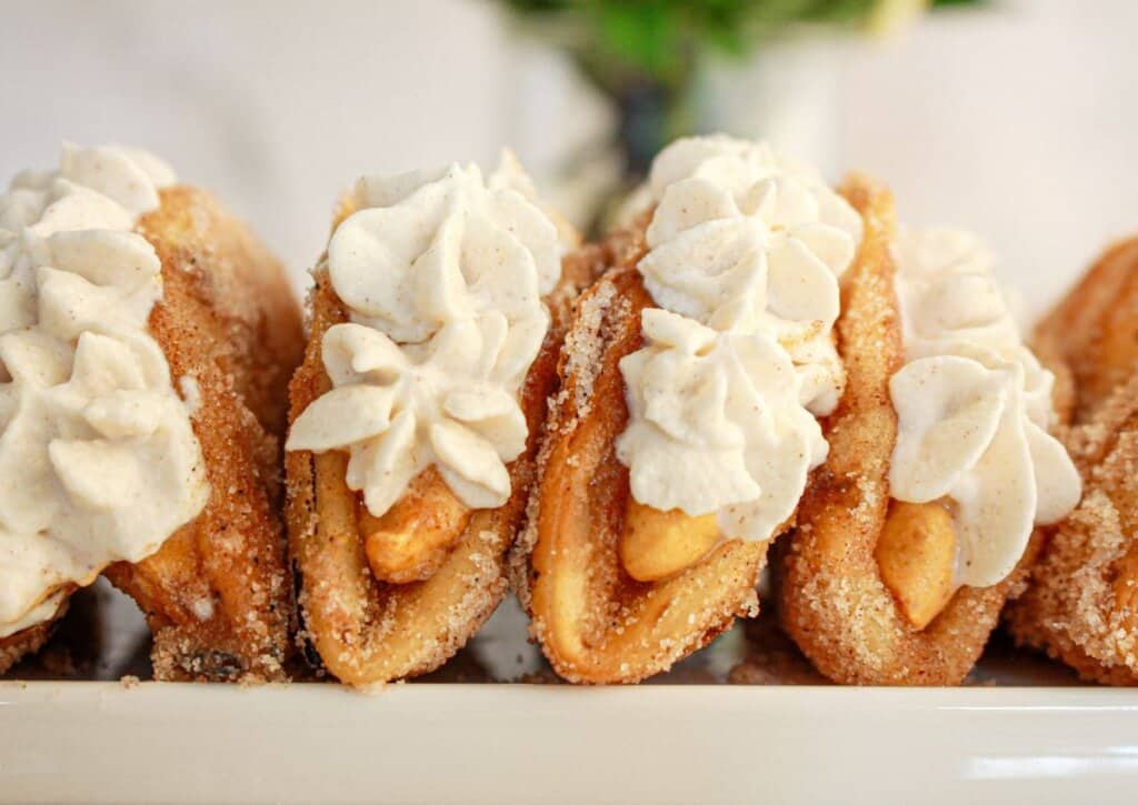Close-up of several churro tacos filled with cream and arranged in a row on a white plate.