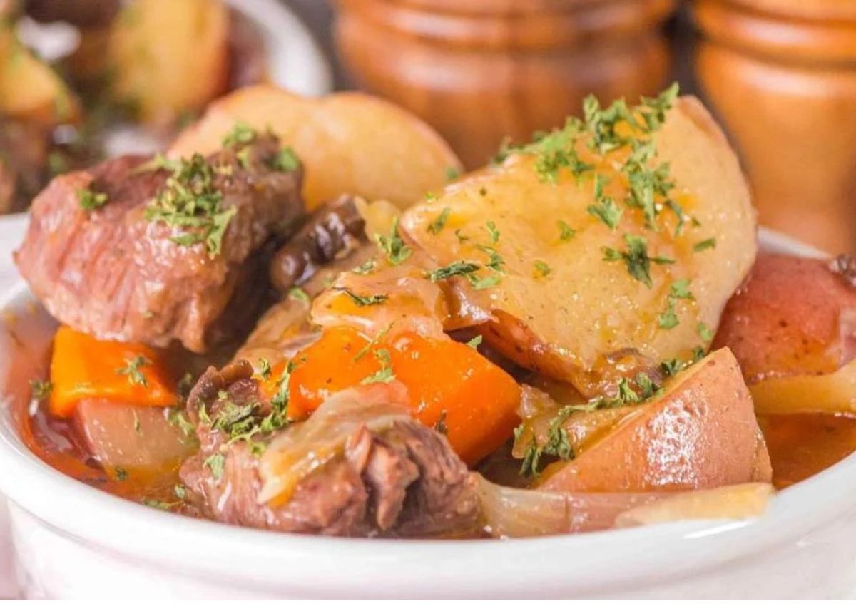 A bowl of beef stew with chunks of beef, potatoes, carrots, and onions, garnished with chopped parsley.