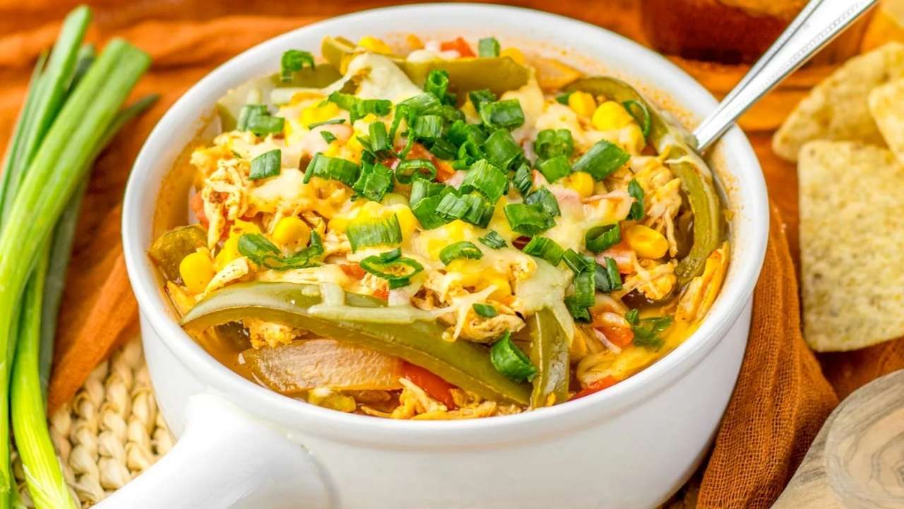 Bowl of chicken fajita soup topped with melted cheese and chopped green onions, with tortilla chips and green onions on the side.
