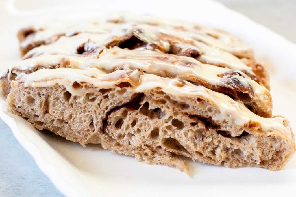A close-up of a cinnamon scone topped with a layer of white icing, served on a white plate.