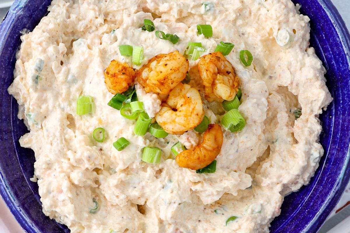 A blue bowl filled with creamy dip, topped with cooked shrimp and chopped green onions.