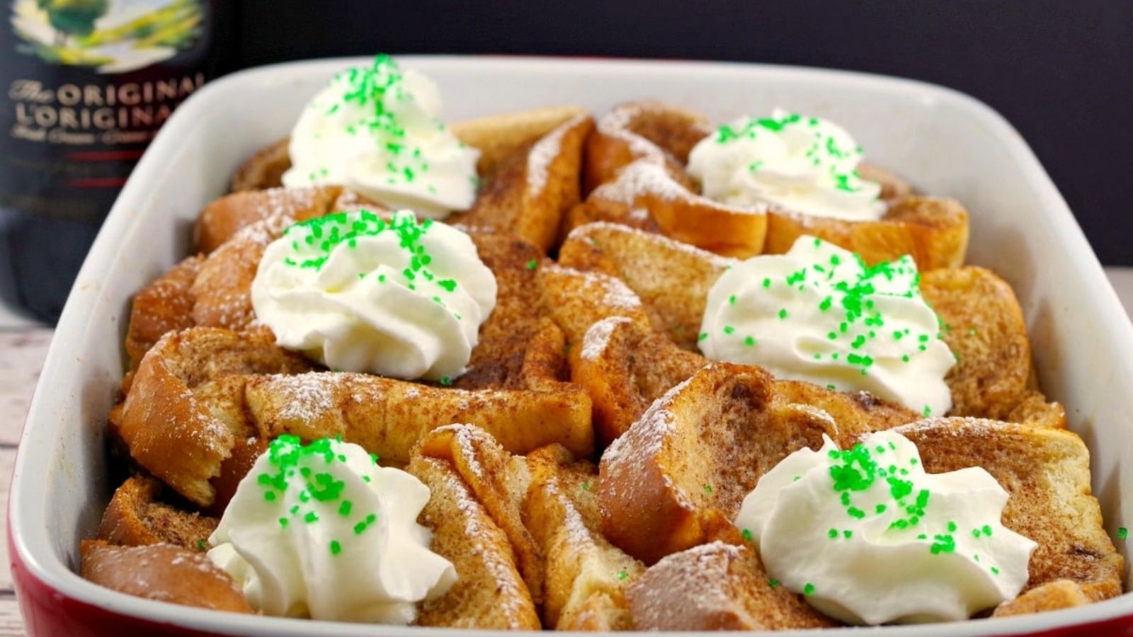 A baking dish filled with slices of French toast, topped with dollops of whipped cream and green sprinkles.