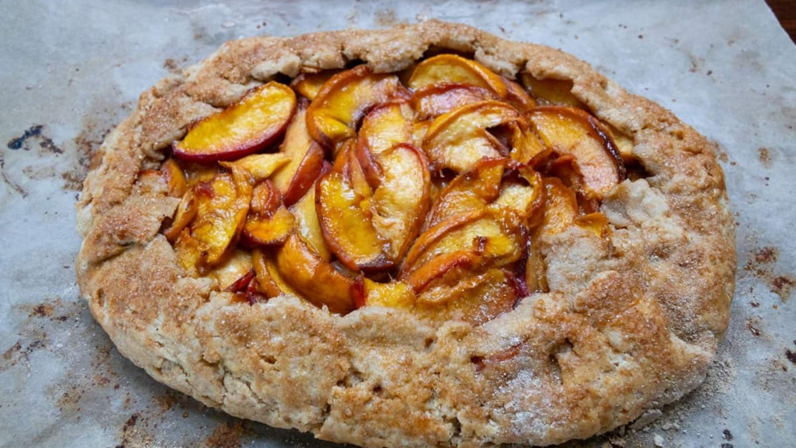 A rustic peach galette with a golden, flaky crust and sliced peaches on top, sitting on parchment paper.