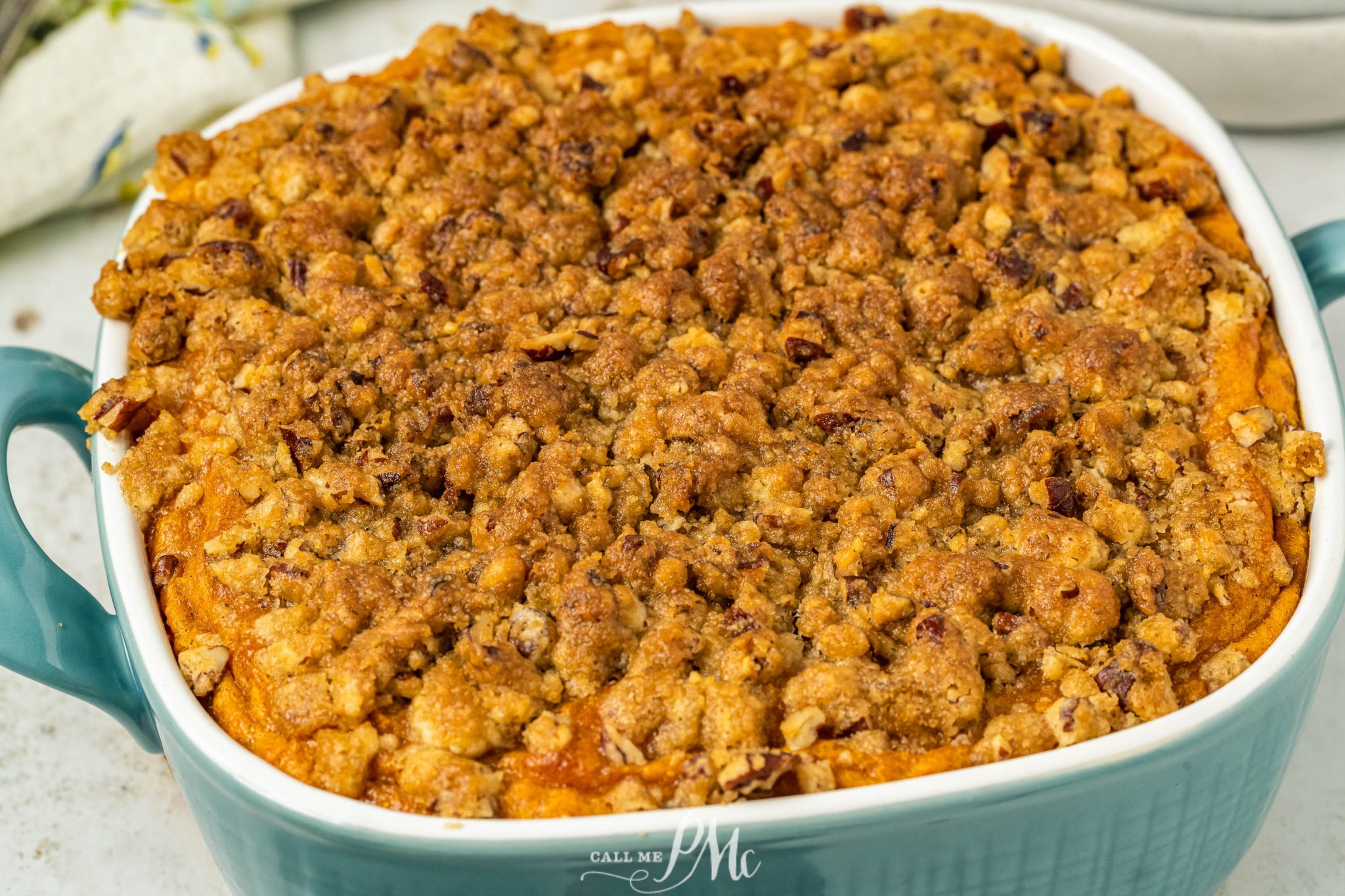 A baked sweet potato casserole with a golden, crumbly pecan topping in a teal square dish.