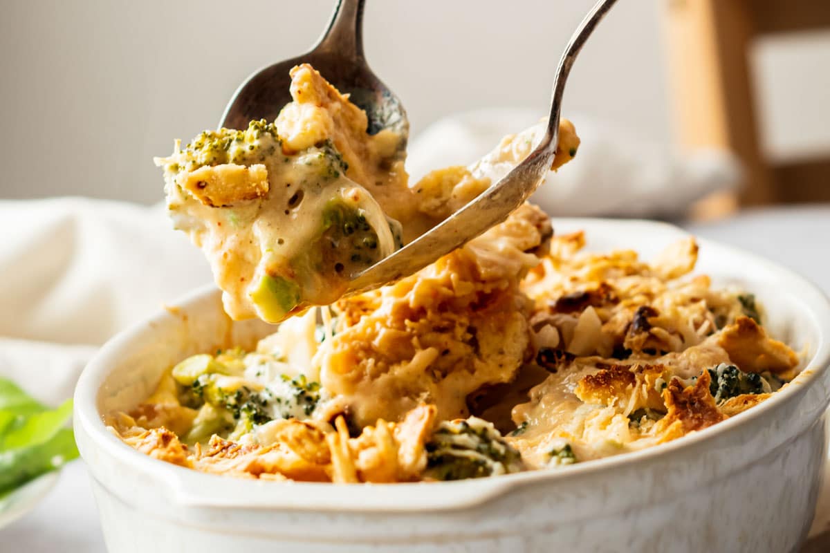 A spoon scooping a serving of cheesy broccoli casserole from a white baking dish.