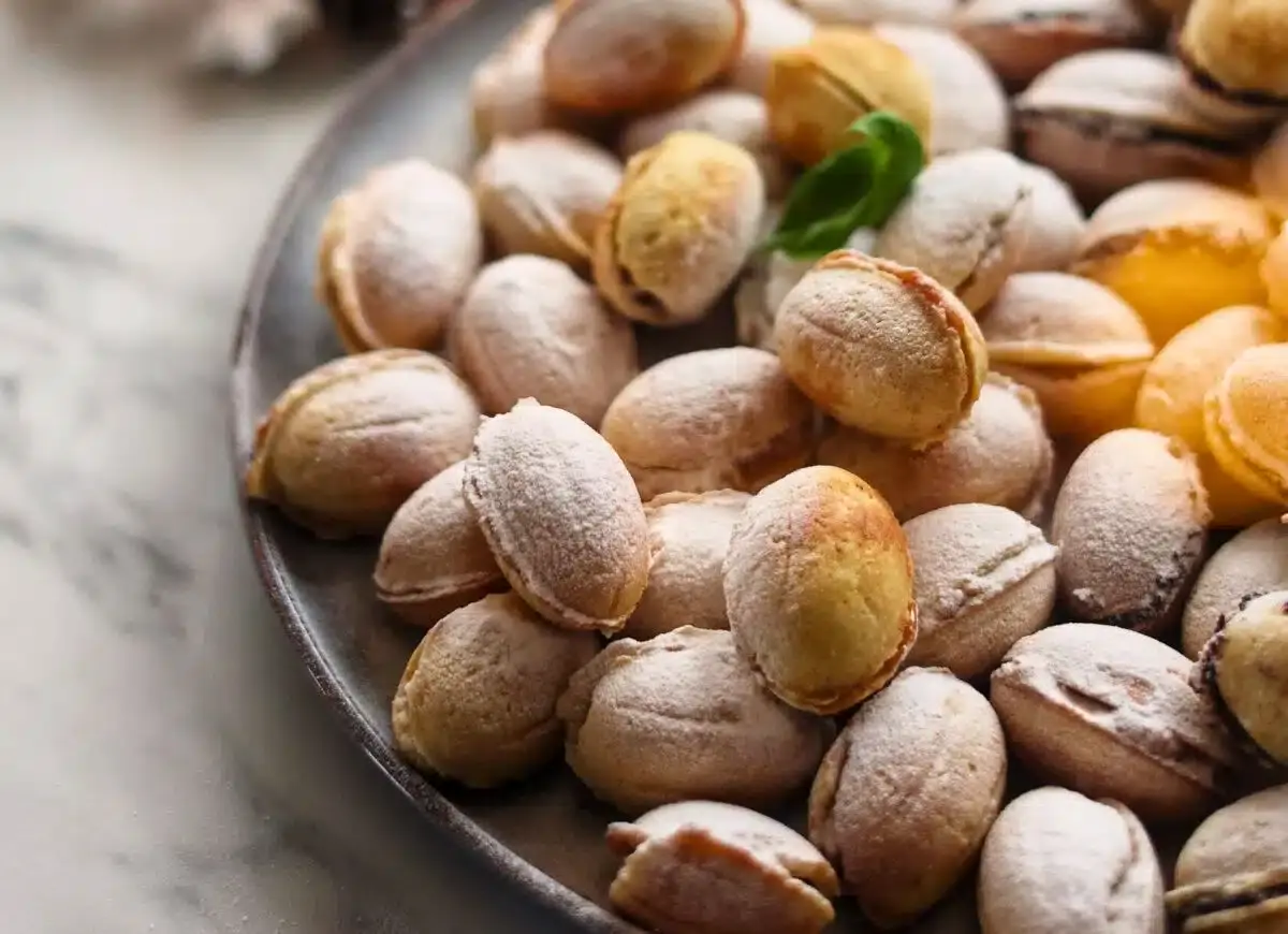 A plate of small, oval-shaped sandwich cookies dusted with powdered sugar, arranged closely together with a sprig of greenery.