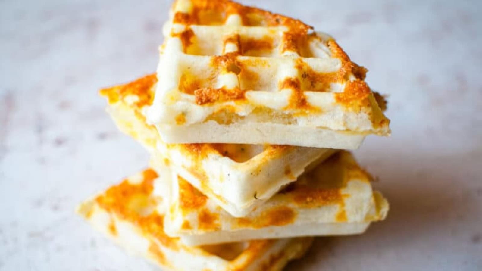 Three golden-brown waffle quarters are stacked on a light surface.