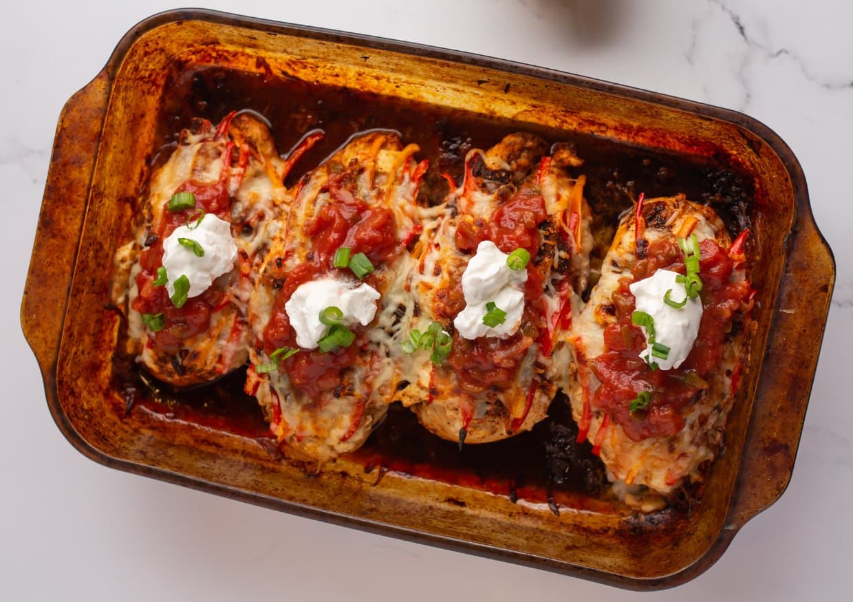 Four baked stuffed chicken breasts topped with melted cheese, salsa, sour cream, and chopped green onions in a rectangular baking dish.