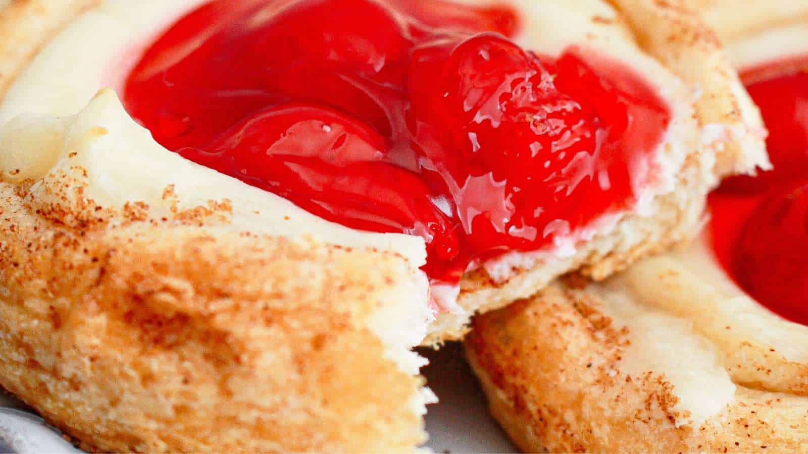 Close-up of a pastry with a crumbly crust, creamy filling, and glossy cherry topping.