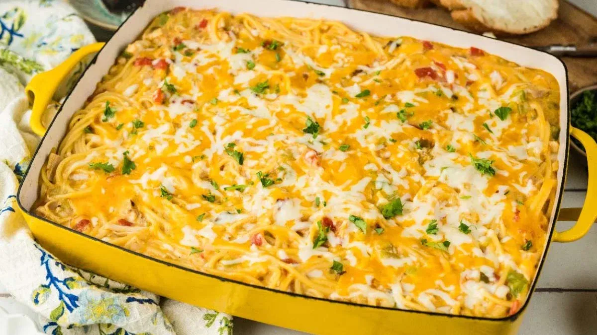 A baked casserole dish filled with spaghetti topped with melted cheese and garnished with chopped herbs.