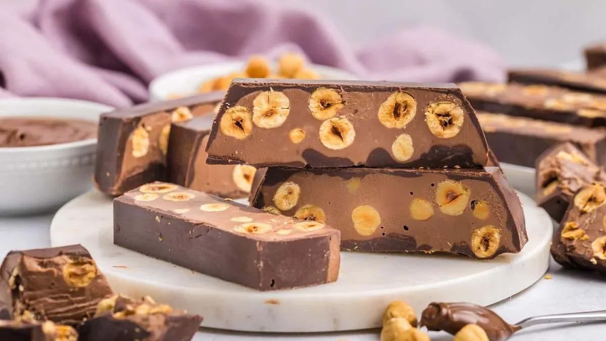 Chocolate and hazelnut nougat bars are stacked on a round marble tray, with whole hazelnuts visible inside the chocolate layers.