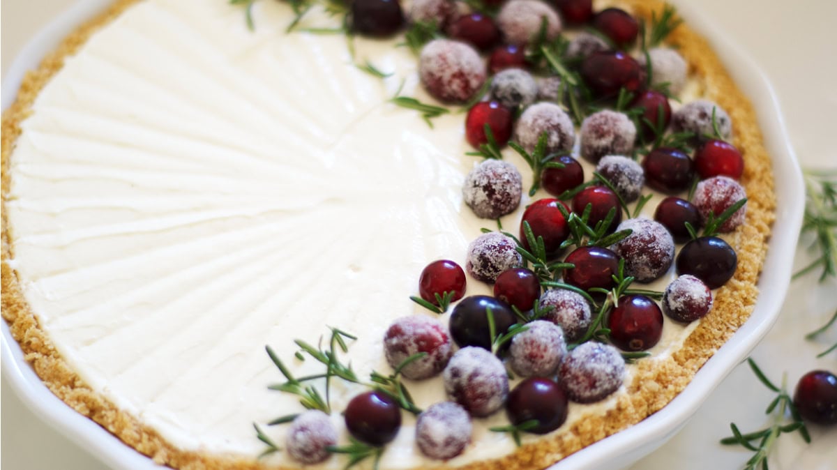 A pie with a creamy white filling, garnished on one side with sugared cranberries and green herb sprigs, in a white dish.
