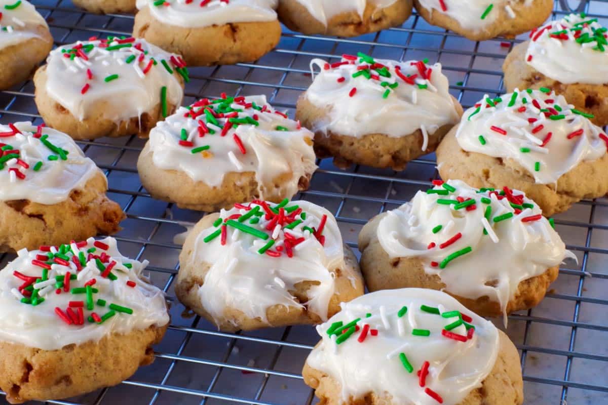 Cookies with white frosting and red, green, and white sprinkles are cooling on a wire rack.