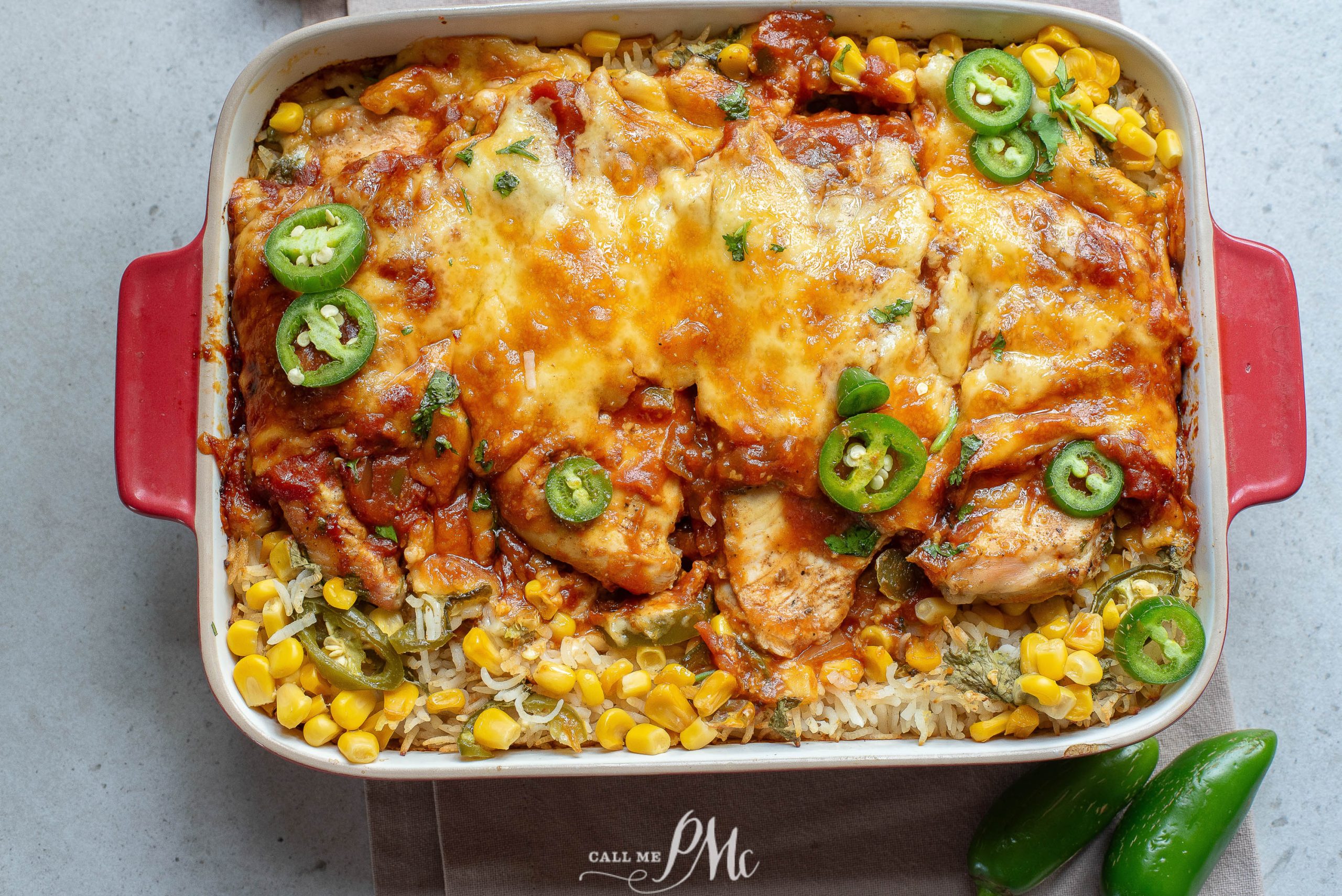A baked casserole dish filled with cheesy chicken, corn, rice, tomato sauce, and topped with sliced jalapeños.