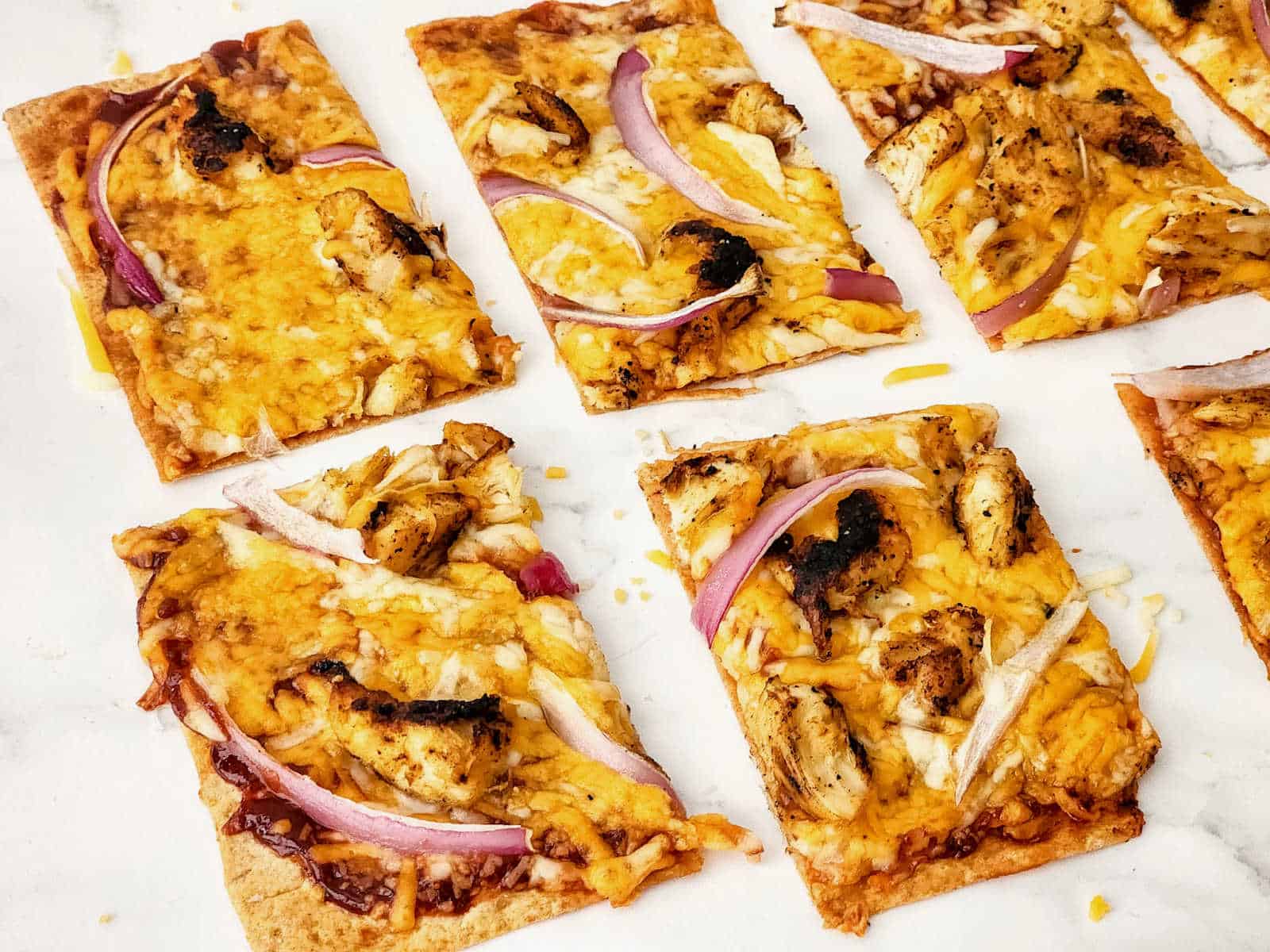 A group of square pizzas with onions and cheese.