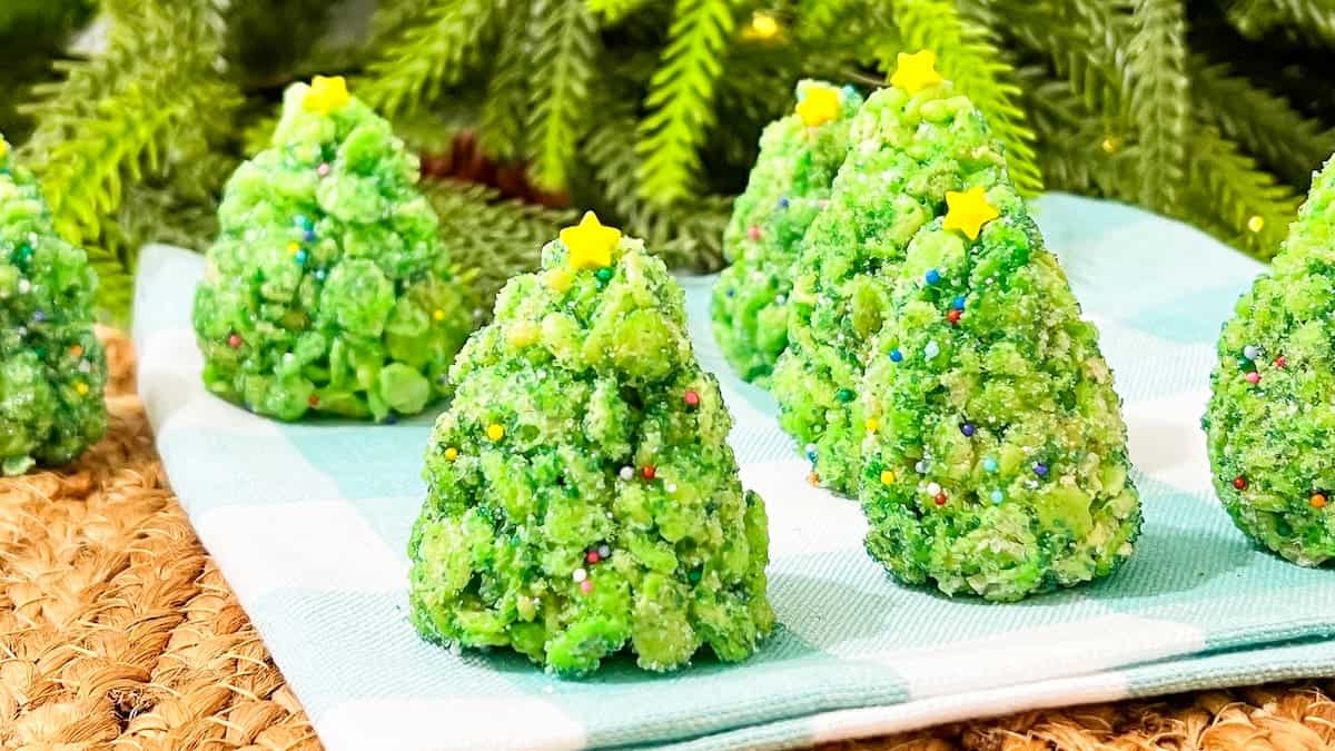 Green Christmas tree-shaped treats with star sprinkles on top, arranged on a blue and white checkered napkin, with green foliage in the background.