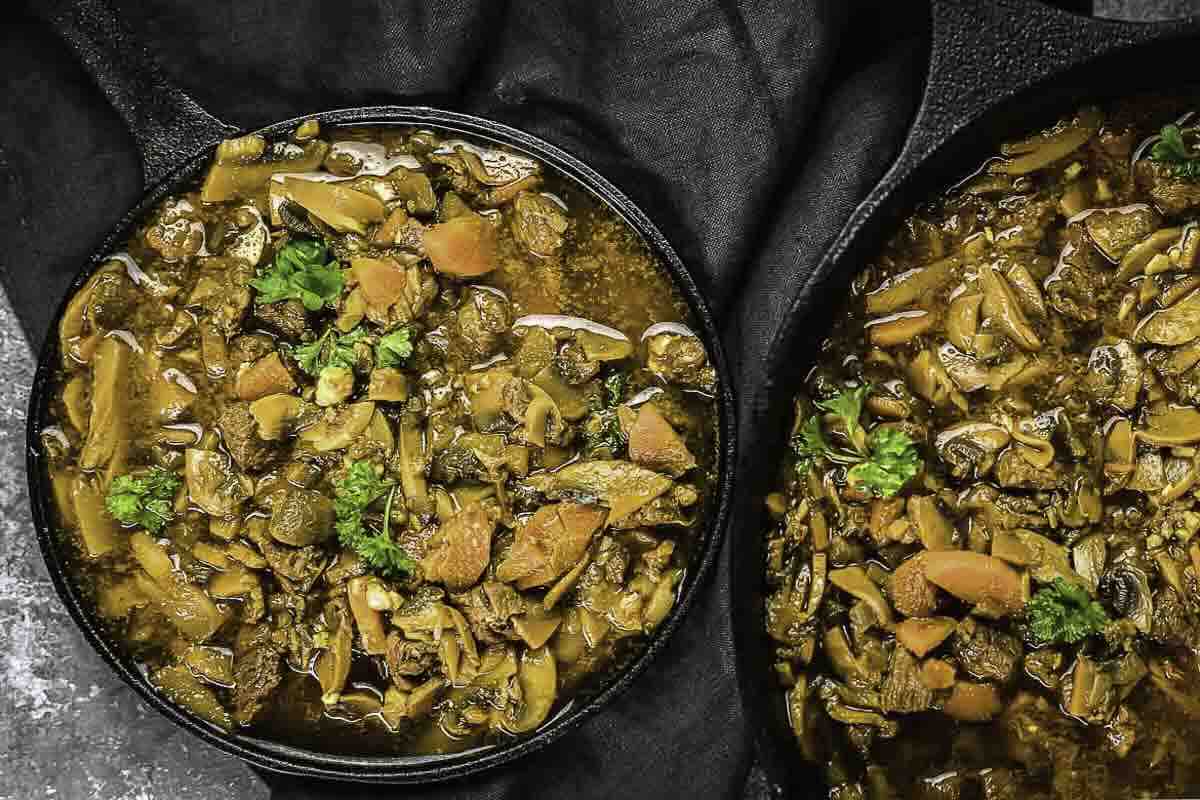 Two black bowls filled with beef stew containing chunks of beef, carrots, mushrooms, and garnished with fresh parsley on a dark background.