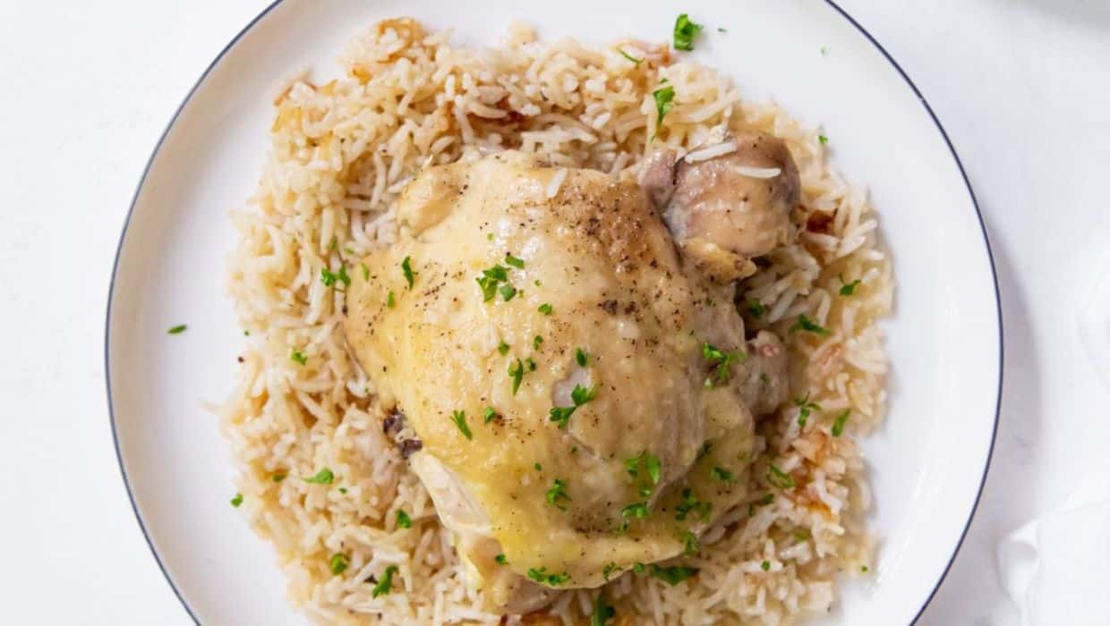 Cooked chicken thigh served on a bed of rice, garnished with chopped parsley on a white plate.