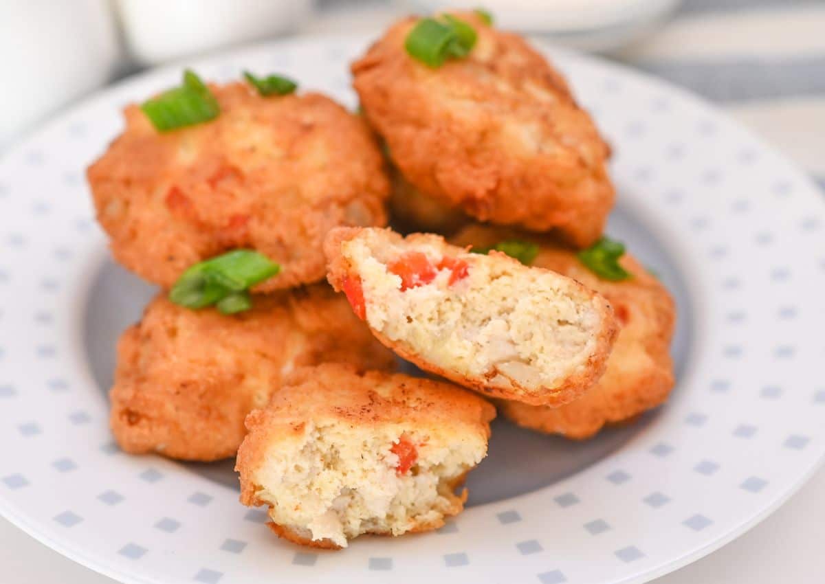A plate of golden-brown fritters garnished with chopped green onions, with one fritter cut in half to show a filling with red and white ingredients.
