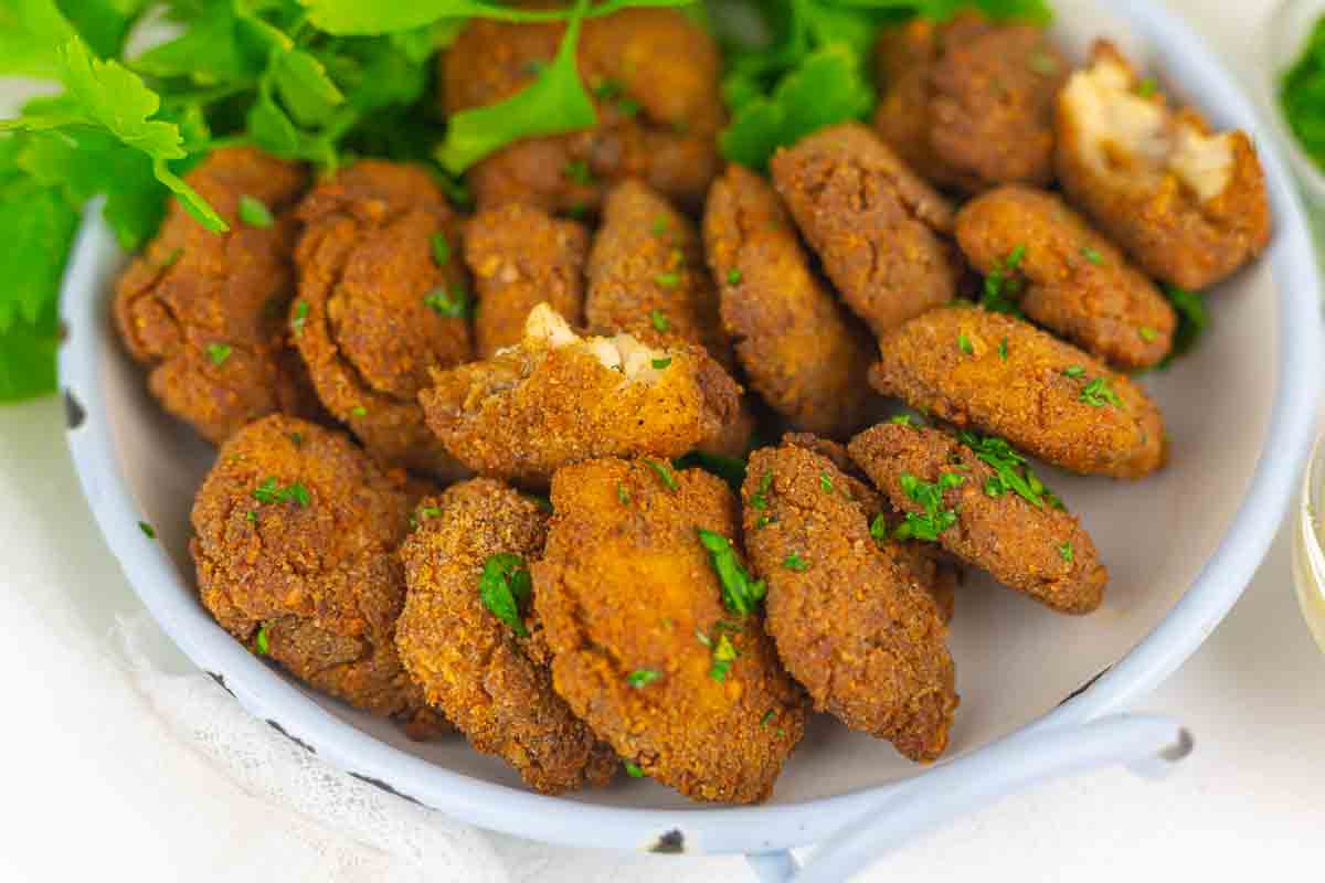 A plate of golden-brown fried fritters garnished with chopped fresh herbs, with leafy greens in the background.