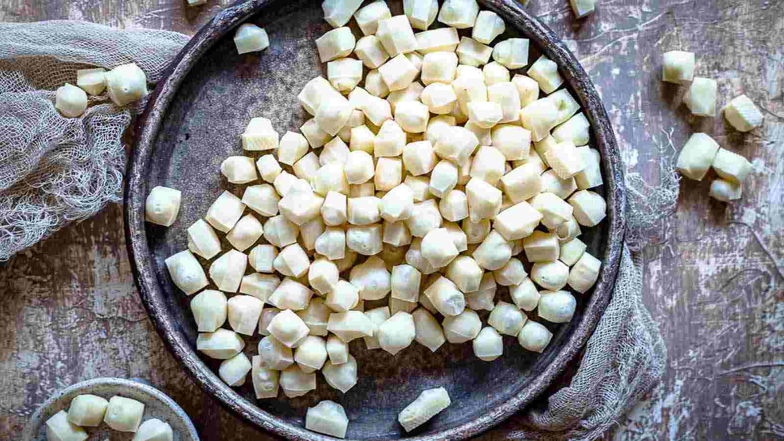 A round dish filled with small, uncooked, handmade gnocchi pieces sits on a textured surface with bits of cloth nearby.