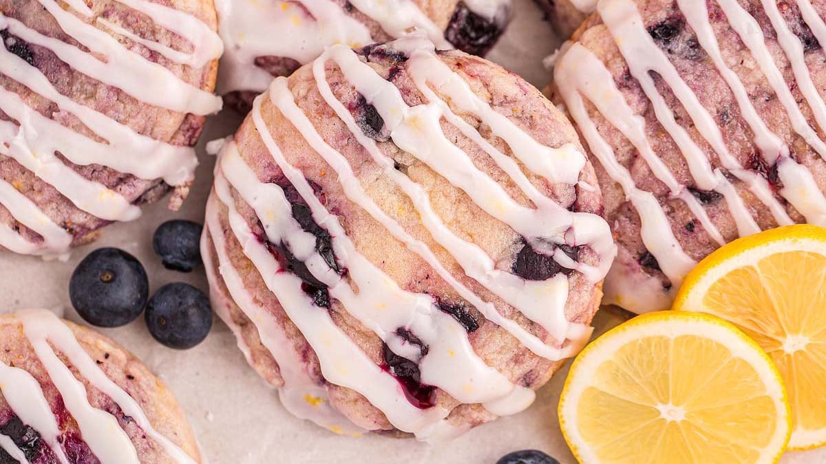 A close-up of iced blueberry scones topped with white glaze, surrounded by fresh blueberries and lemon slices.