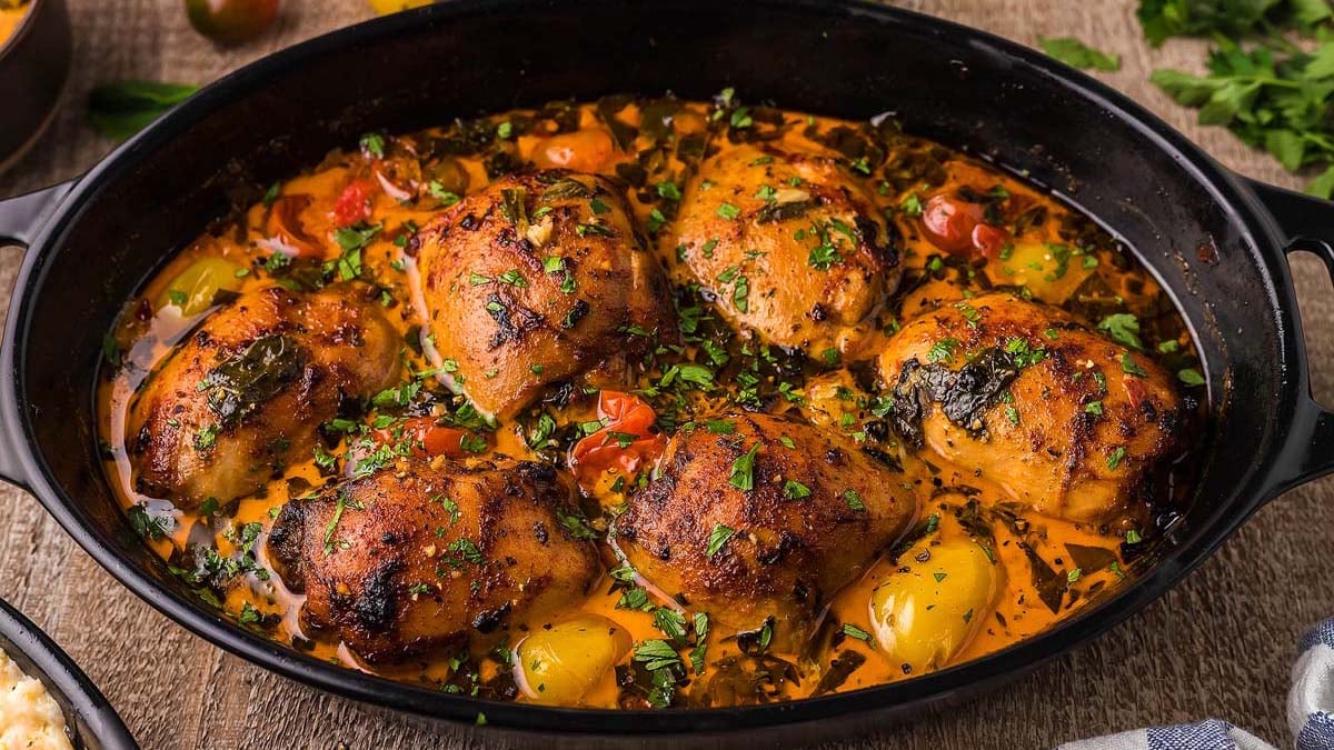 Roasted chicken thighs with herbs and vegetables in a black baking dish, garnished with chopped parsley.