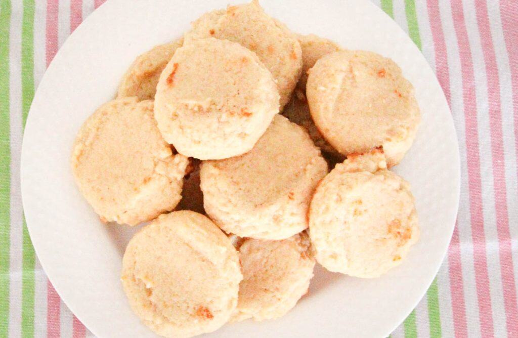 A white plate filled with round, light-colored cookies is placed on a striped pink and green tablecloth.