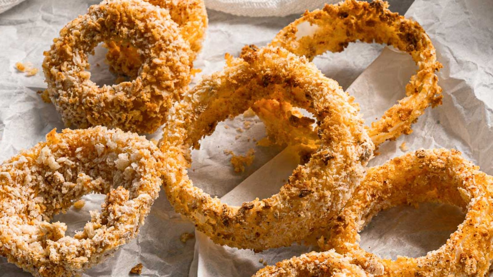 Several crispy, golden-brown onion rings arranged on parchment paper.