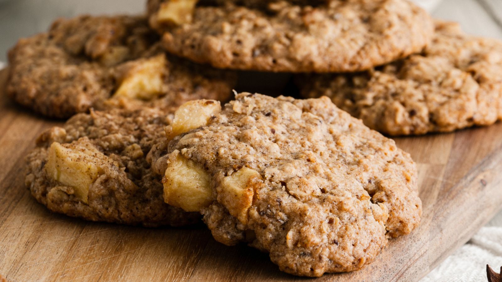 A close-up of several oatmeal cookies with visible chunks of apple on a wooden cutting board.