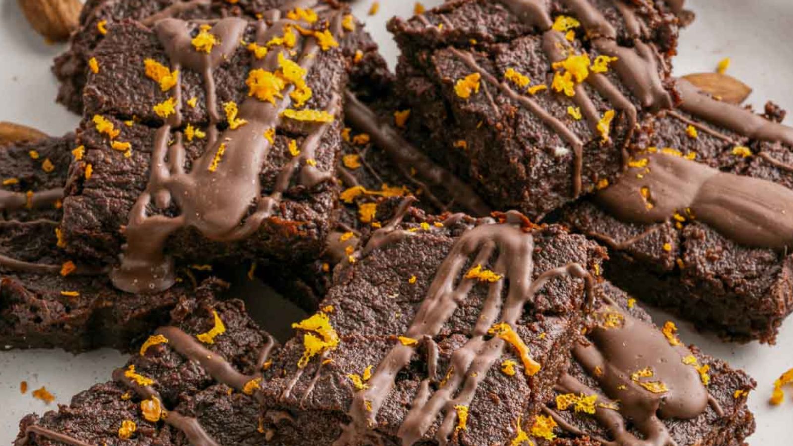 A plate of chocolate brownies topped with chocolate drizzle and orange zest.