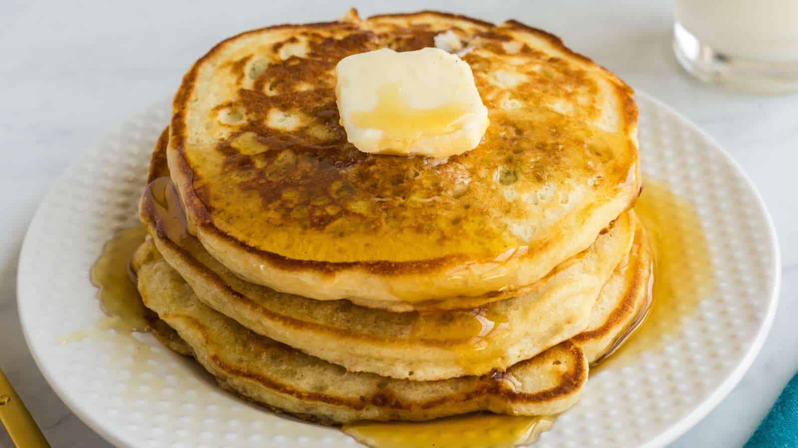 A stack of three pancakes topped with a pat of butter and drizzled with syrup on a white plate.