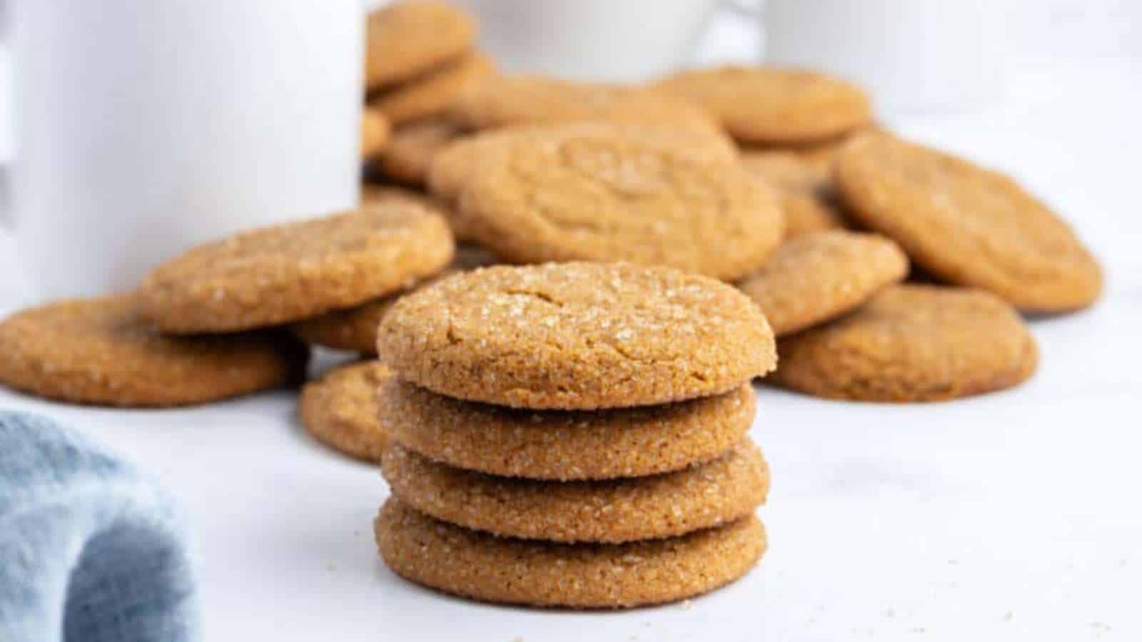 A stack of sugar-coated cookies is placed in front of a scattered pile of similar cookies on a white surface.