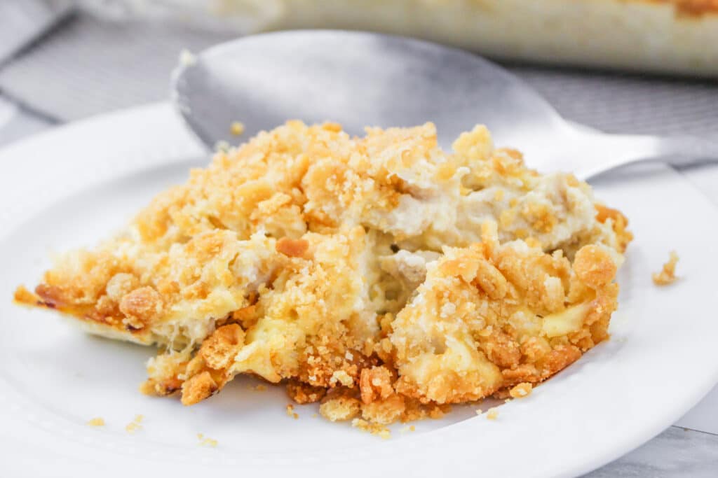 A serving of creamy, crumb-topped casserole on a white plate with a large spoon in the background.