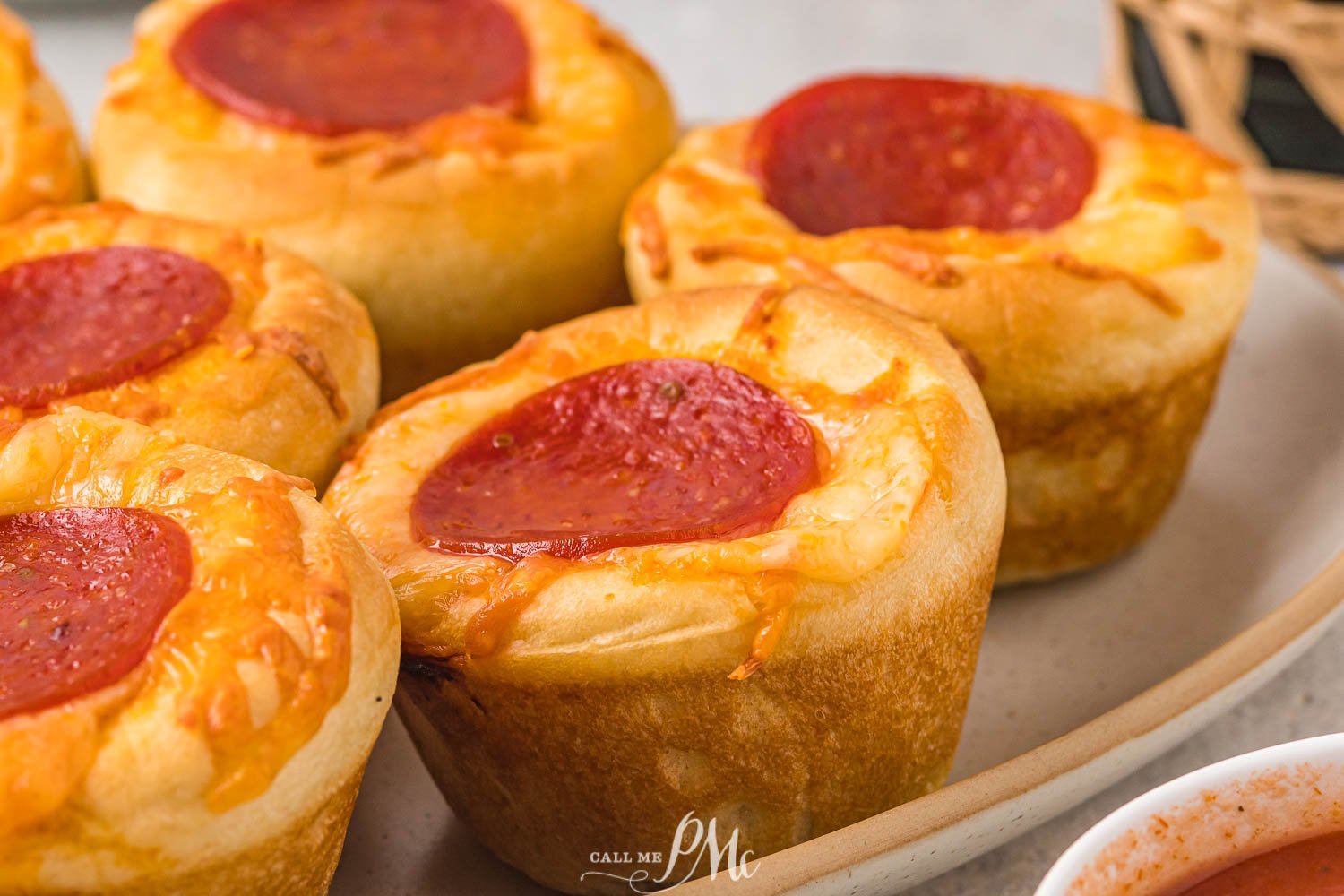 Close-up of several pepperoni pizza muffins on a white plate, each topped with melted cheese and a slice of pepperoni.