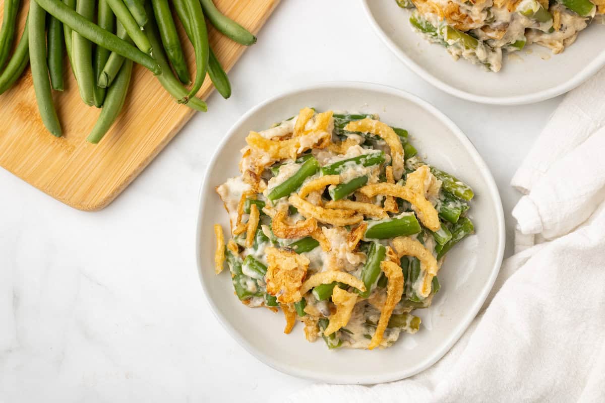A plate of green bean casserole topped with crispy fried onions, with fresh green beans on a cutting board nearby.