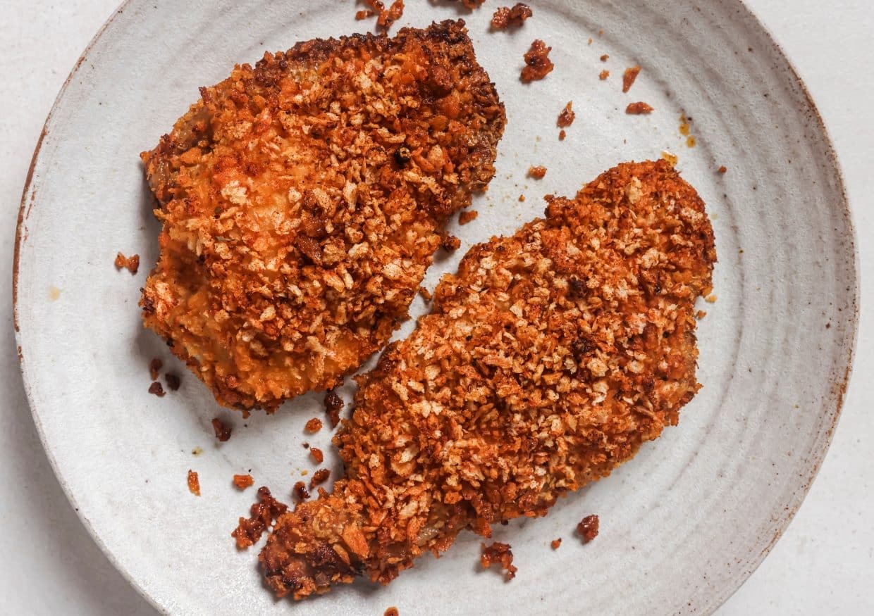 Two pieces of crispy, breaded baked chicken are served on a round, light-colored plate.