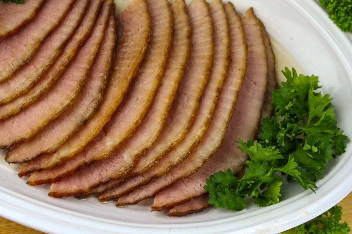 Sliced roast beef arranged on a white plate with sprigs of fresh parsley on the side.