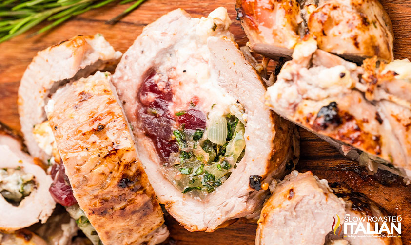 Sliced stuffed pork tenderloin with a filling of cheese, herbs, and cranberries, shown on a wooden surface.