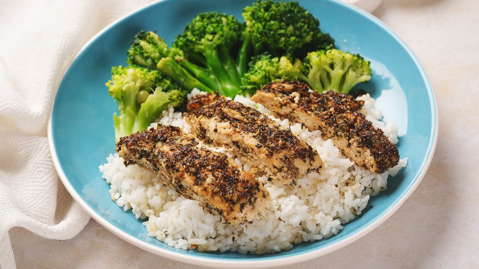 A blue plate with white rice, sliced herb-seasoned chicken breast, and steamed broccoli.