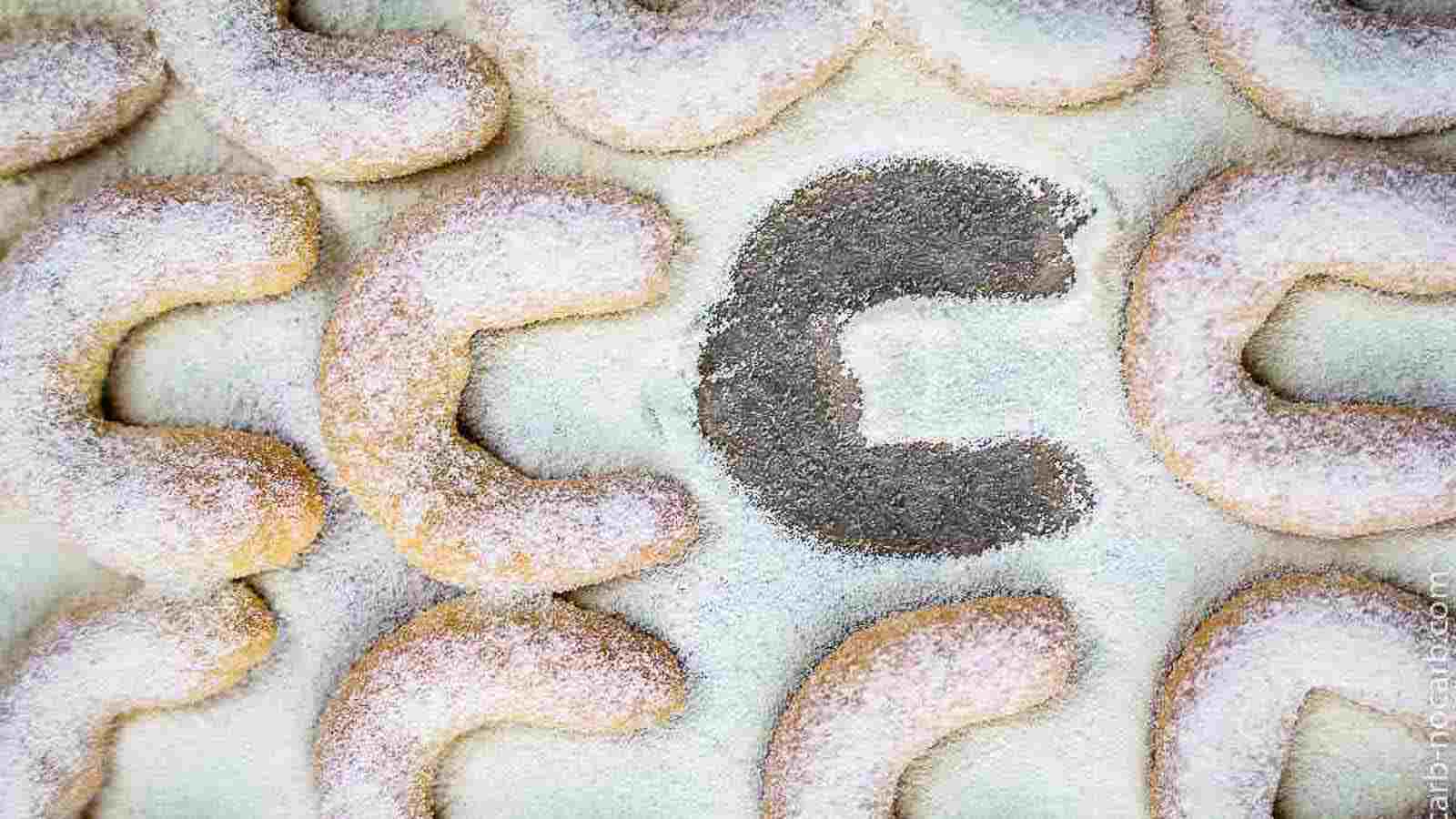 Several crescent-shaped cookies dusted with powdered sugar, with one cookie missing in the center, leaving behind a sugared outline.