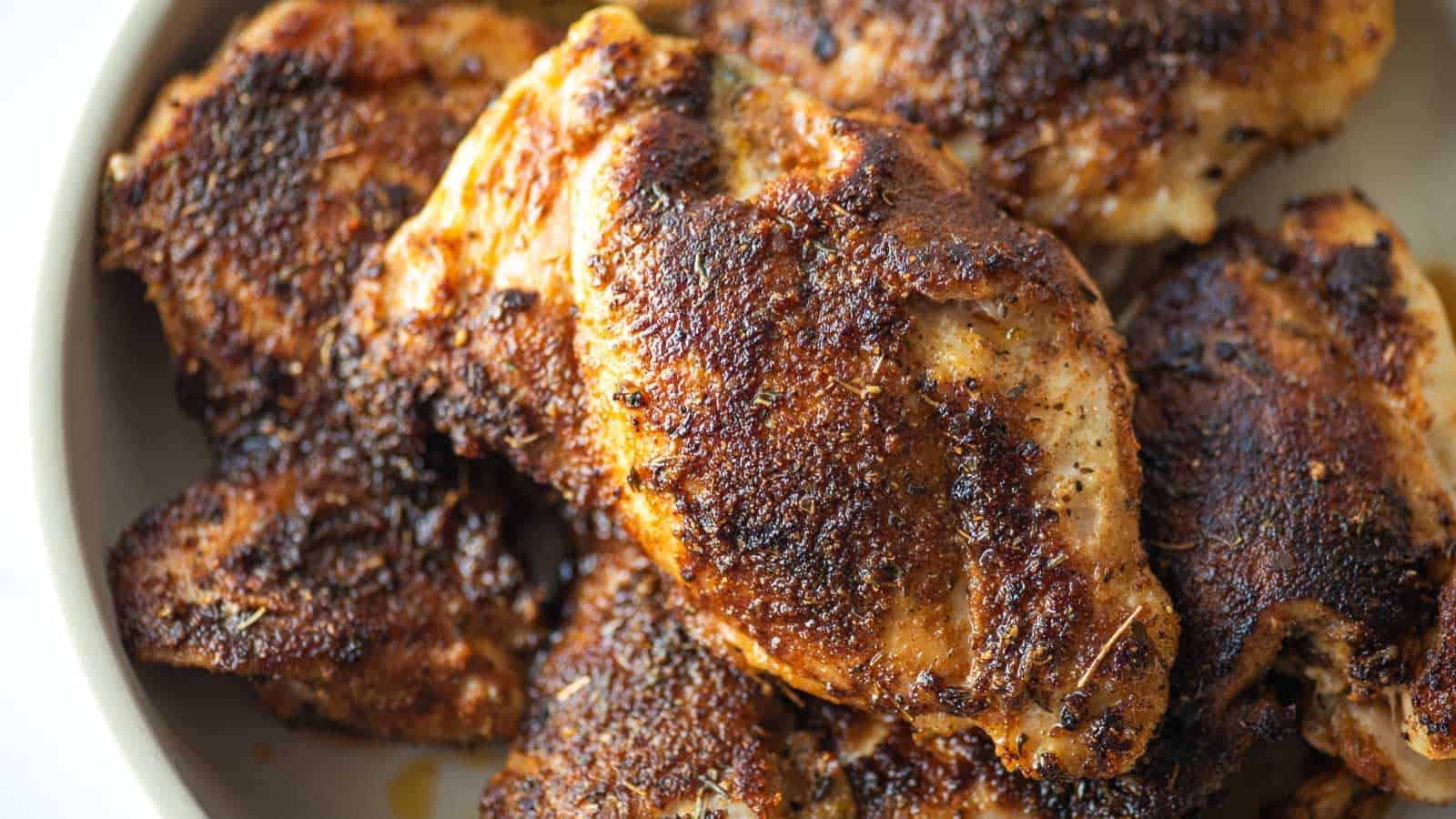 A plate of cooked, seasoned chicken thighs with a crispy, browned exterior.