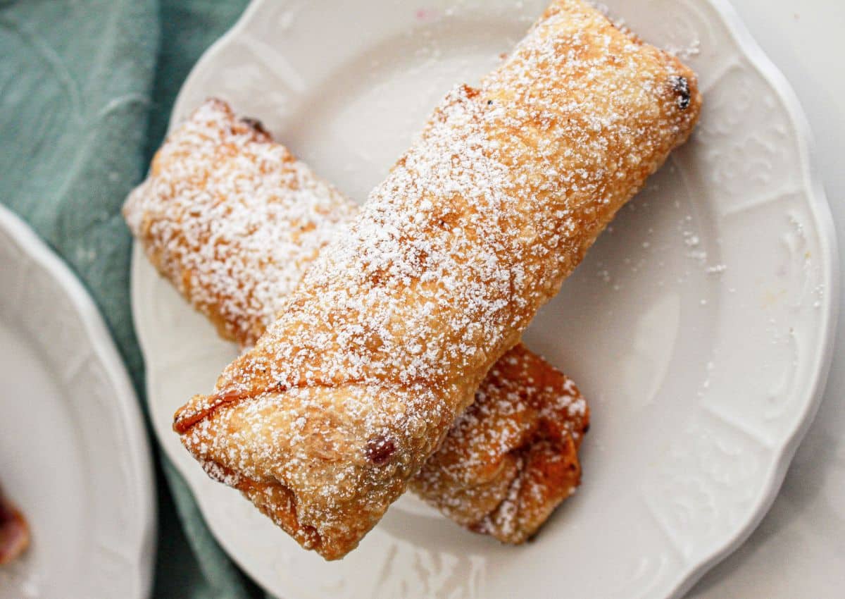 Two fried pastries dusted with powdered sugar are placed on a white plate.
