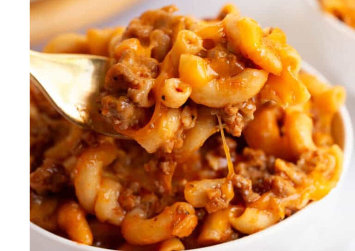 A close-up of a bowl of cheesy macaroni with ground beef, with a fork lifting a portion.
