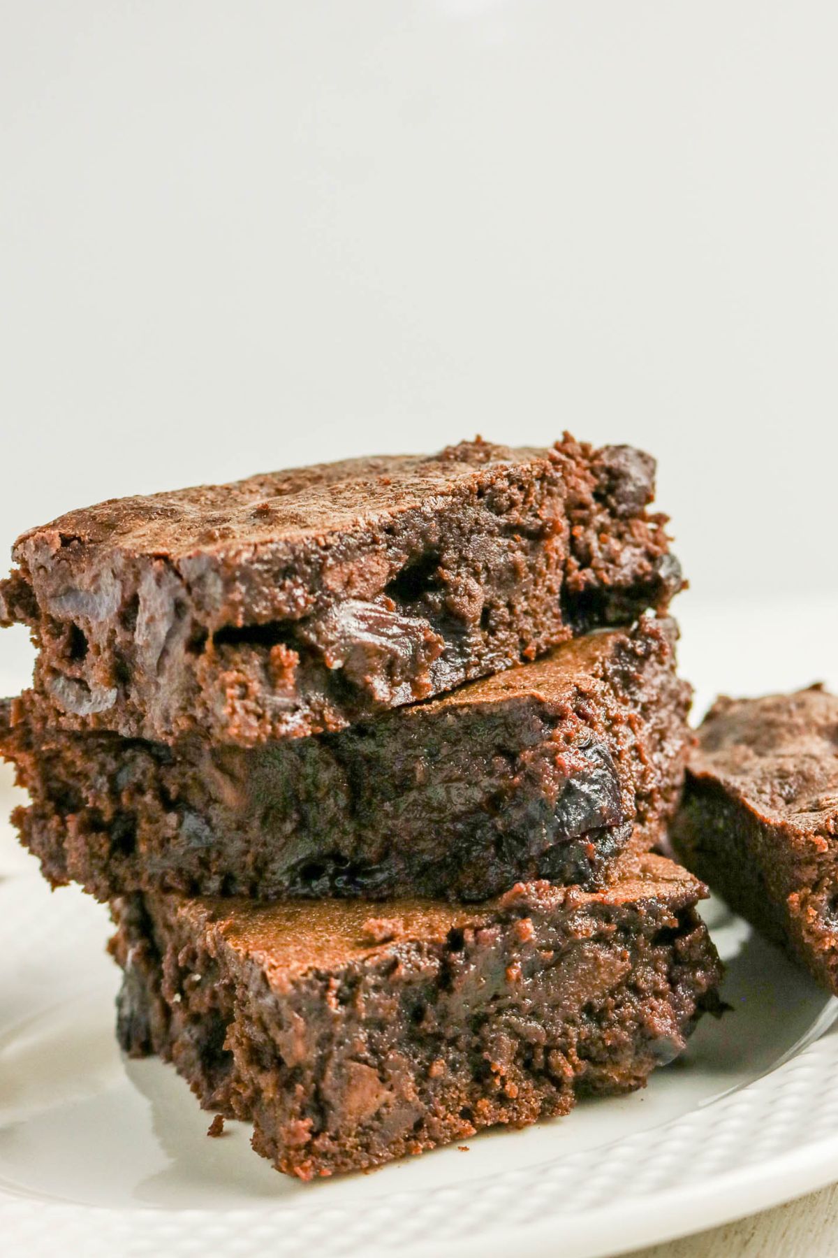 A stack of three thick, chocolate brownies sits on a white plate, showing a moist and fudgy texture.
