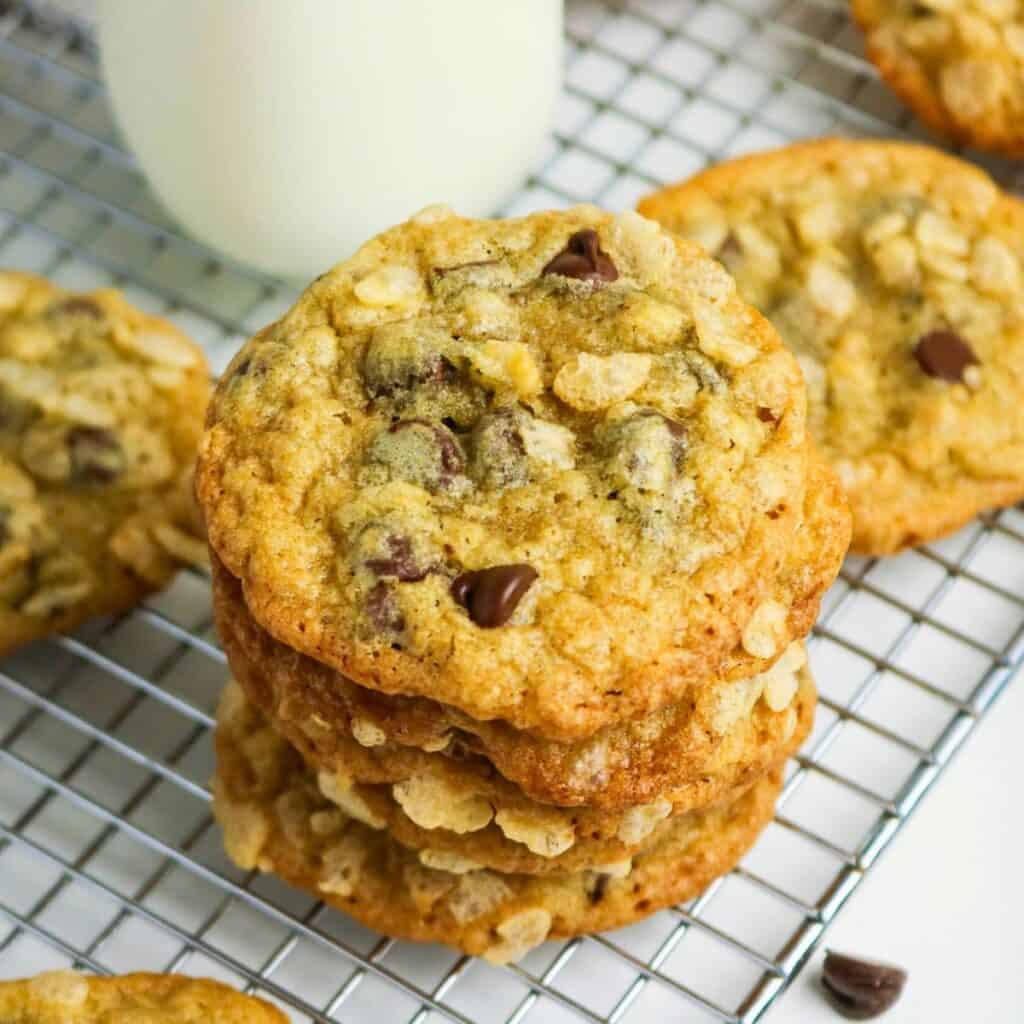 A stack of oatmeal chocolate chip cookies sits on a cooling rack with a glass of milk in the background.