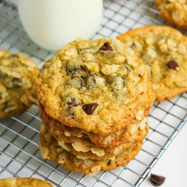 A stack of oatmeal chocolate chip cookies sits on a cooling rack with a glass of milk in the background.