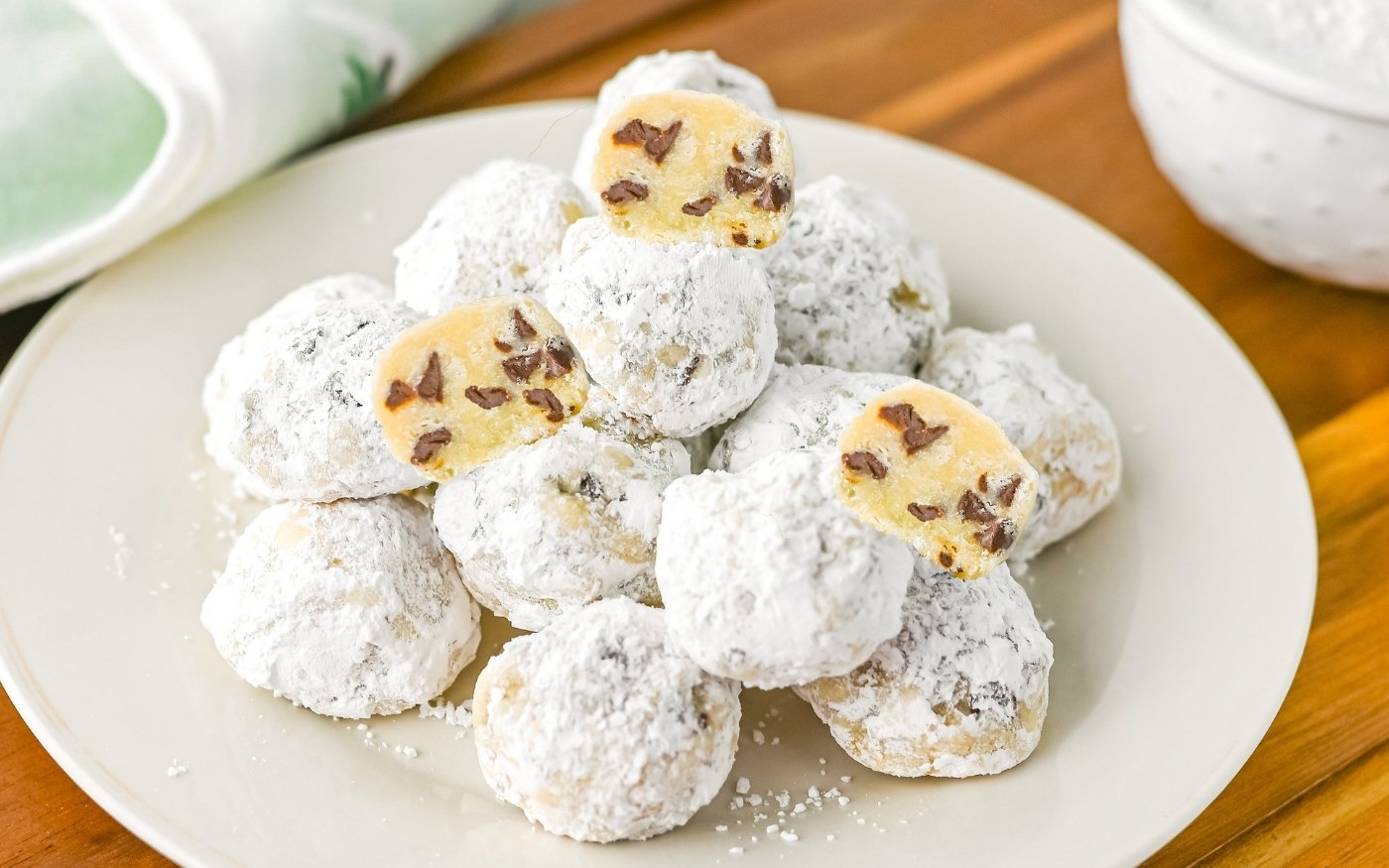 A plate of round cookies coated in powdered sugar, some of which are cut open to show chocolate chips inside.