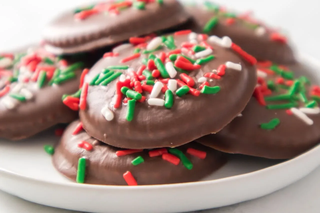 Chocolate-covered cookies topped with red, green, and white sprinkles are stacked on a white plate.