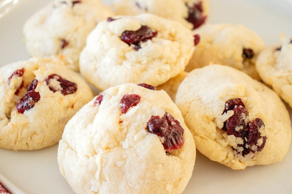 A plate of round, crumbly cookies with visible dried cranberries on a white surface.